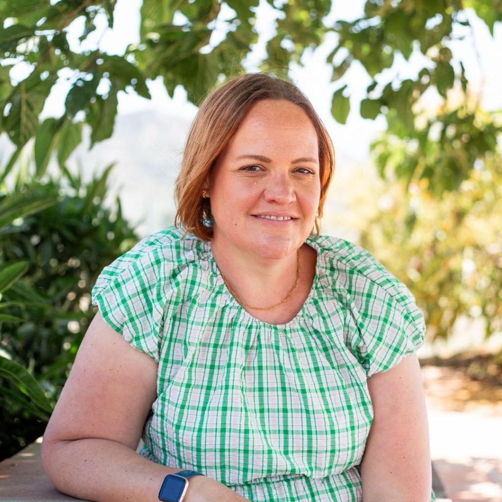 Corinne wearing a green dress and sitting outside, she is smiling at the camera